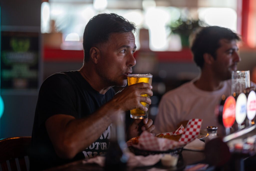 Two patrons sitting at the bar with a beer and food