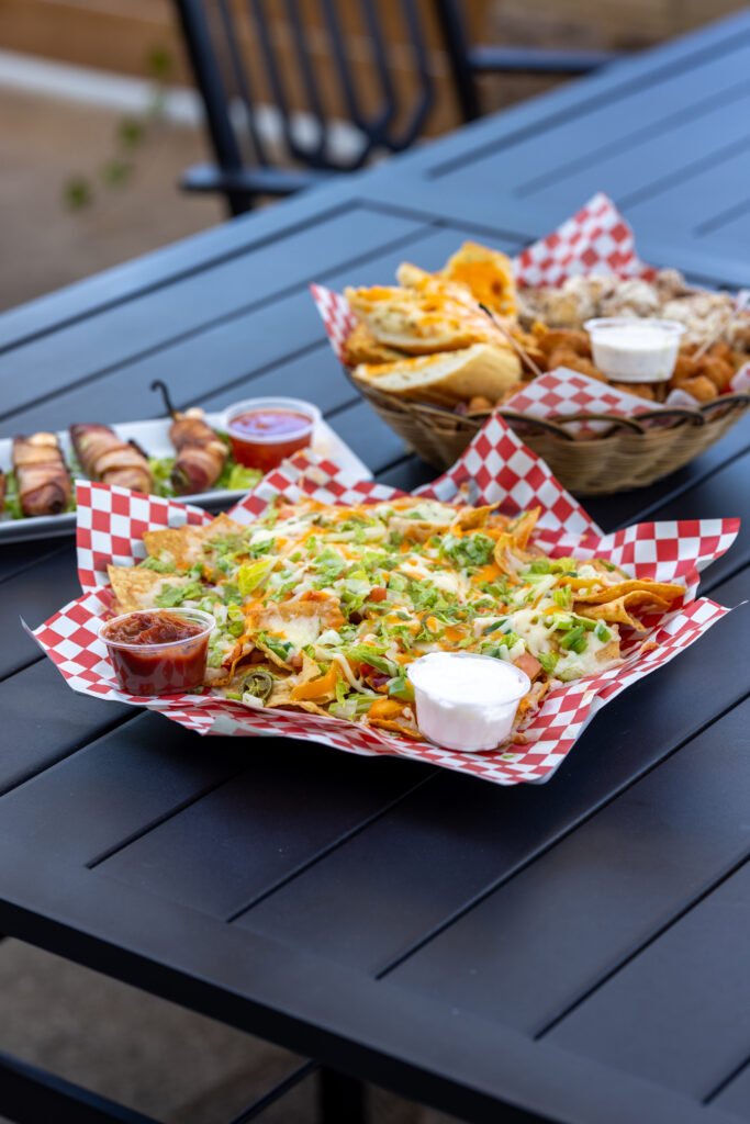 Nachos, poppers and an appetizer basket on a patio table