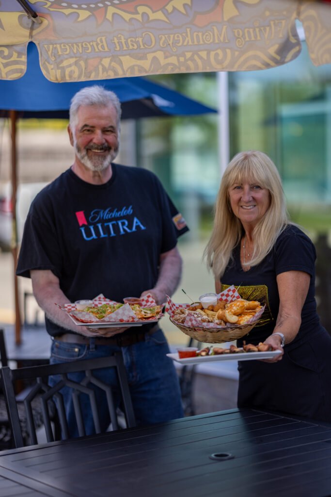 Lori and Gary, owners of The Last Shot, holding food on the patio