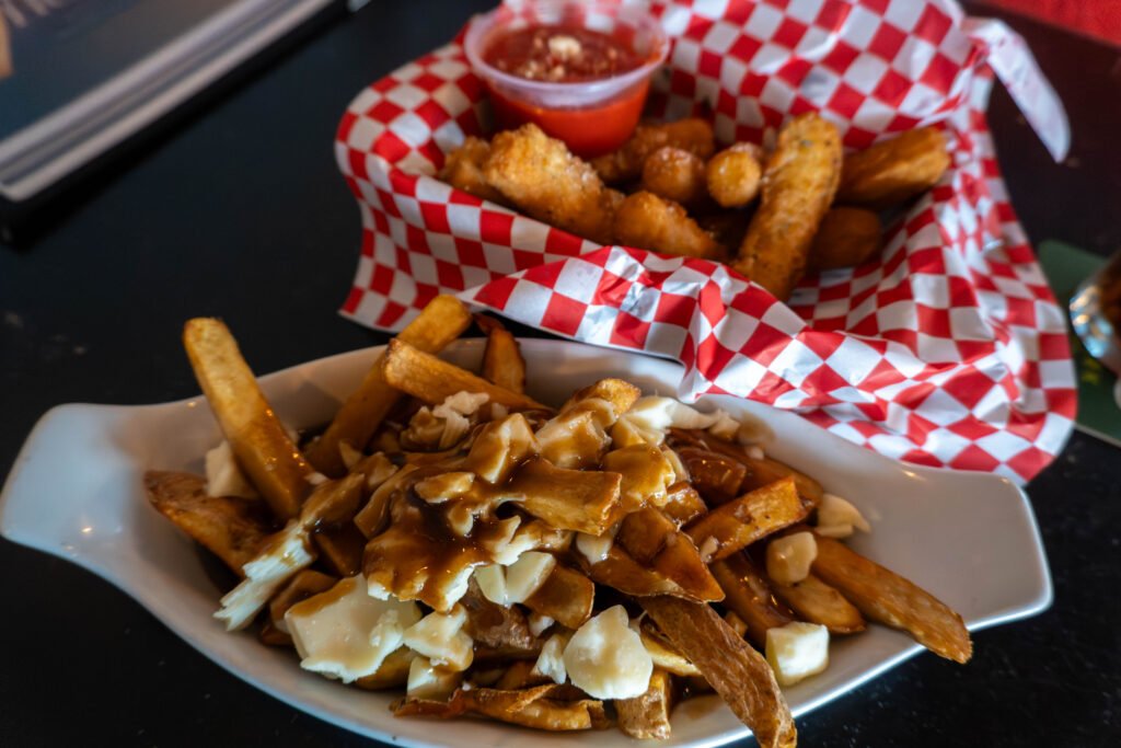 Basket of poutine beside breaded appetizers and dipping sauce